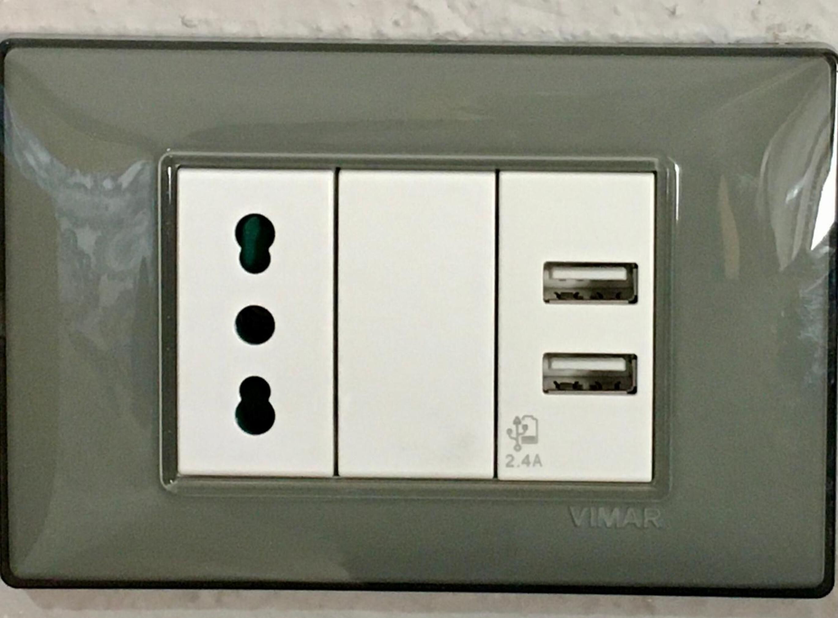 A wall-mounted electrical outlet with three switches and two USB ports, labeled "VIMAR".