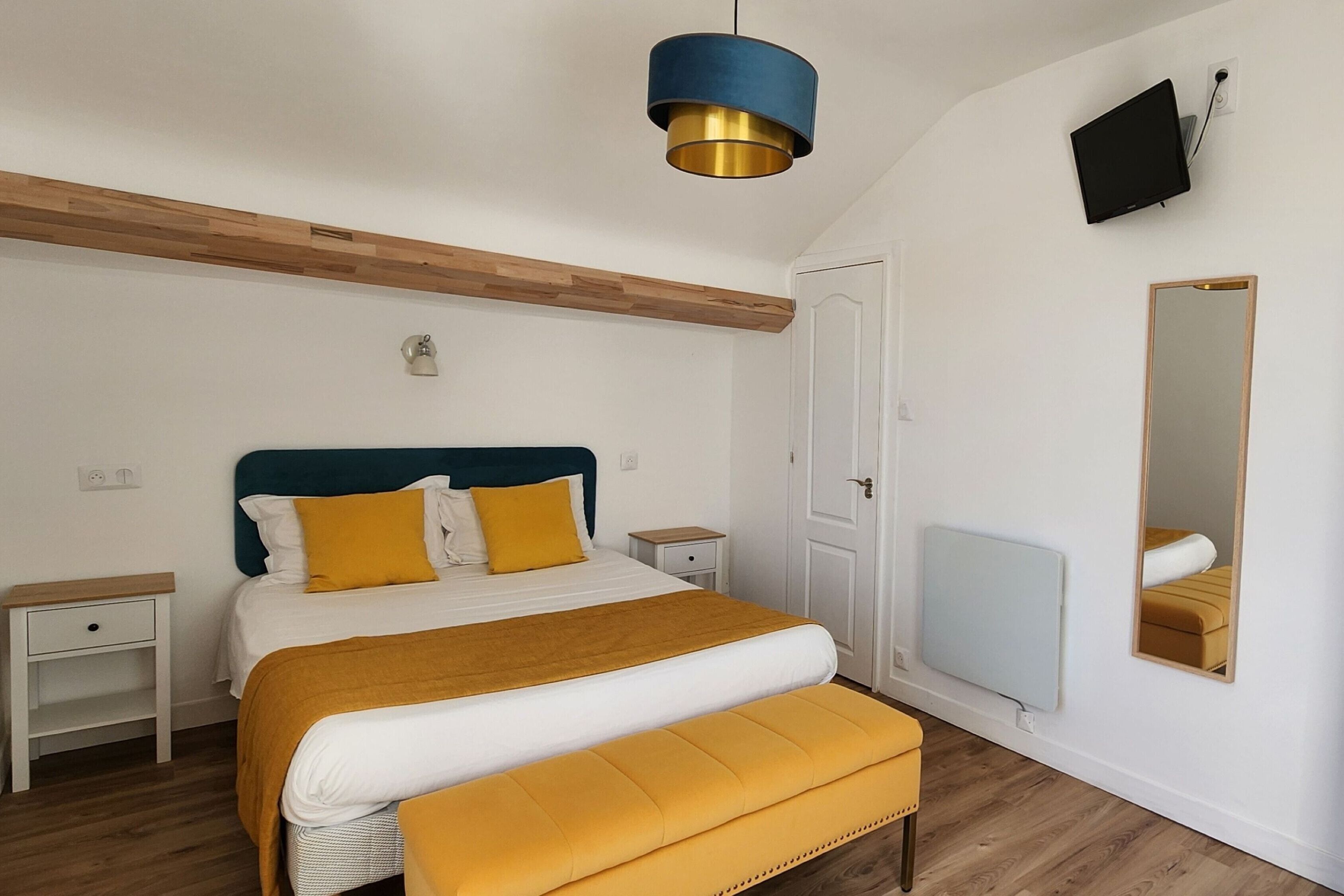 Een slaapkamer met een bed, nachtkastjes, een spiegel, een televisie en een plafondlamp.
