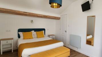 Een slaapkamer met een bed, nachtkastjes, een spiegel, een televisie en een plafondlamp.