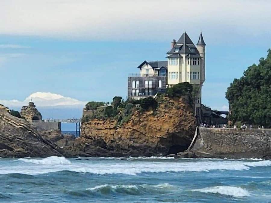Um edifício à beira-mar com uma torre, cercado por ondas e surfistas.