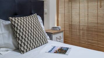 A neatly made bed with a magazine, a patterned pillow, and a bedside table with a phone.