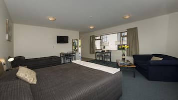 A hotel room with a large bed, a sofa, a desk with a chair, a TV mounted on the wall, and a window with curtains.