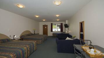 A hotel room with two single beds, a sofa, a dining table with a basket of breakfast items, and a mirror on the wall.