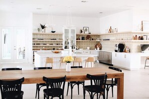 Una cocina moderna con armarios blancos, una isla central con sillas y una mesa de comedor con sillas.