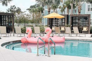 A swimming pool with pink flamingo floats, lounge chairs, and a yellow umbrella. - Clean, Cozy & Chic Apartment. CDC Cleaning Standards! Just 3 Miles From Disney (Kissimmee)