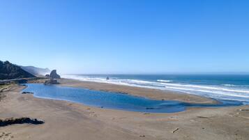 A beach with a clear sky, a rocky outcrop, and calm waves.