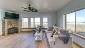 Ein Wohnzimmer mit Kamin aus Stein, Deckenventilator, großem Fenster mit Blick auf den Strand, Sofa und Couchtisch.