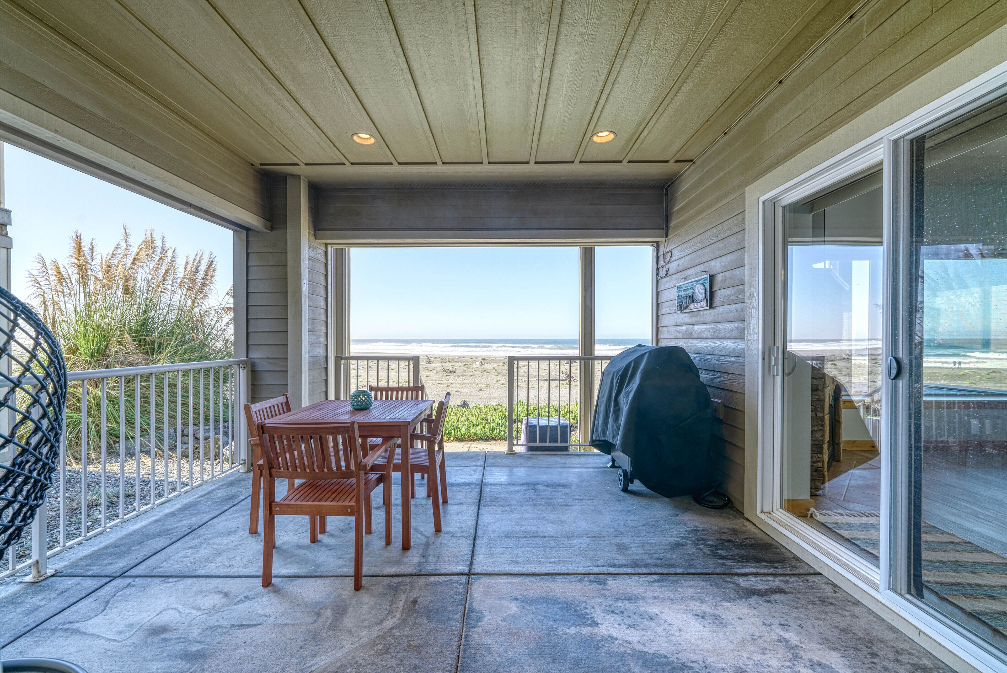 Une terrasse couverte avec une table et des chaises, un barbecue et une vue sur la plage.