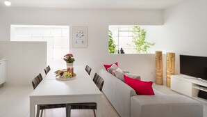 Un soggiorno moderno e luminoso con zona pranzo, un divano con cuscini rossi, una televisione e un'ampia finestra con vista sul verde.