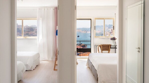 A hotel room with two beds, a balcony with a view of the sea, and a desk with a chair.