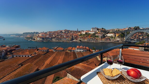 Una terrazza con un tavolo apparecchiato per un pasto, affacciata su una vista urbana che include un fiume e un ponte.