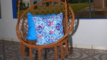 Relax in a cozy swing chair suspended from the ceiling, overlooking a serene outdoor view through a window with a blue frame.