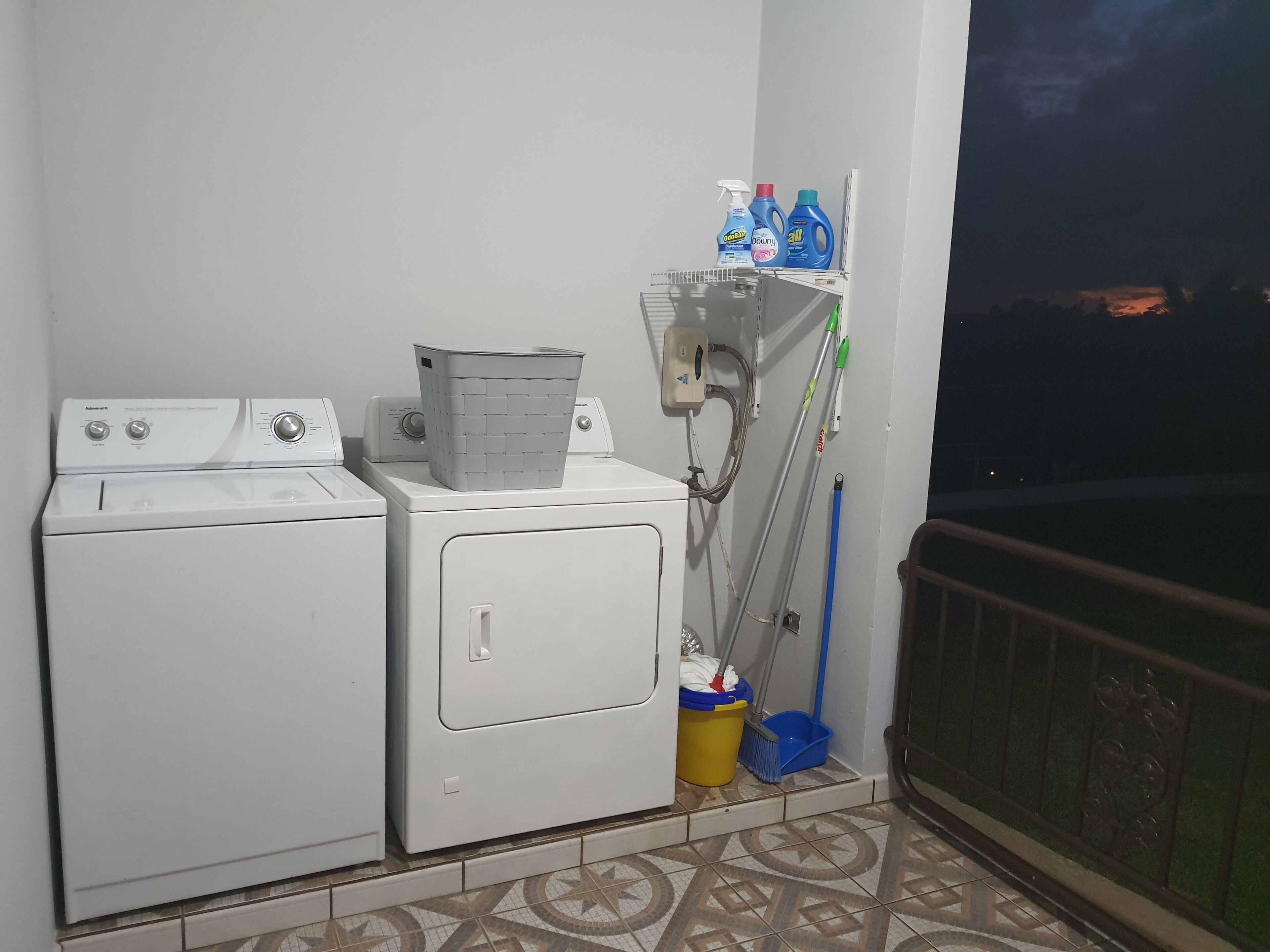 A laundry area with two washing machines, a drying rack, cleaning supplies, and a mop.