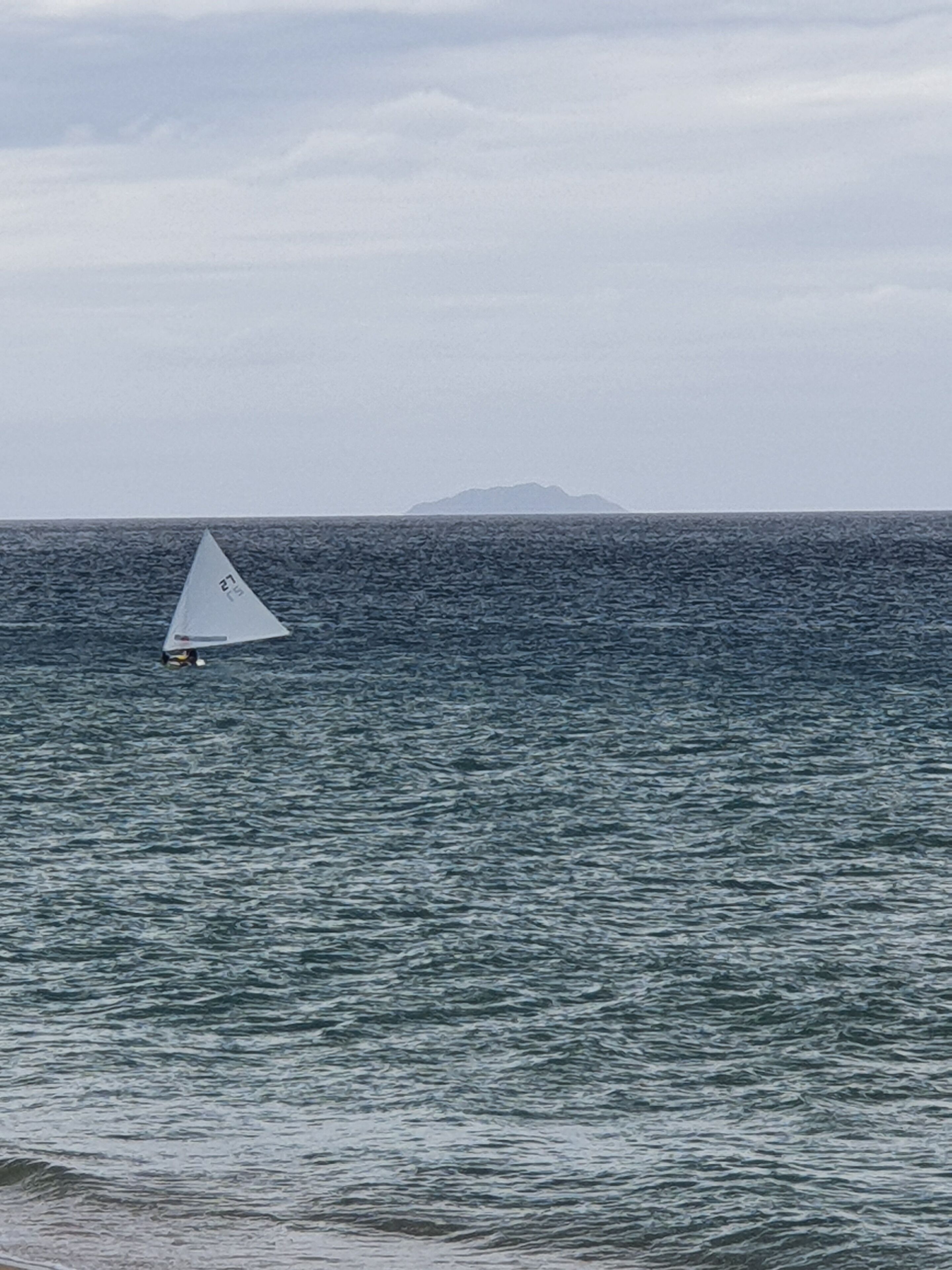 Un velero en un mar tranquilo con una isla distante.