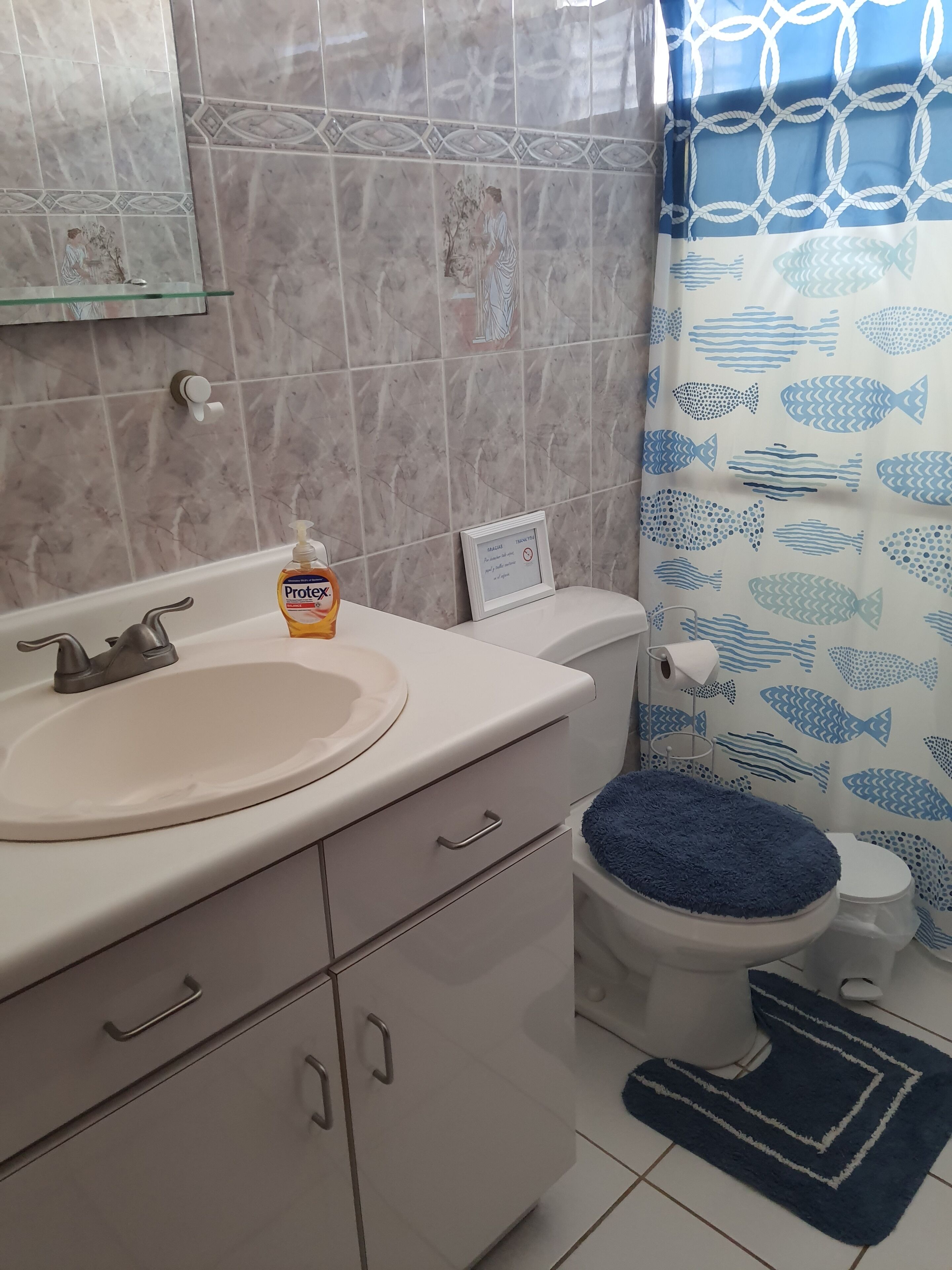 Un bagno con lavandino, wc e tenda della doccia con motivo a pesce.