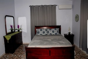 A bedroom with a wooden bed, a dresser, a mirror, a nightstand, and a wall-mounted air conditioner.
