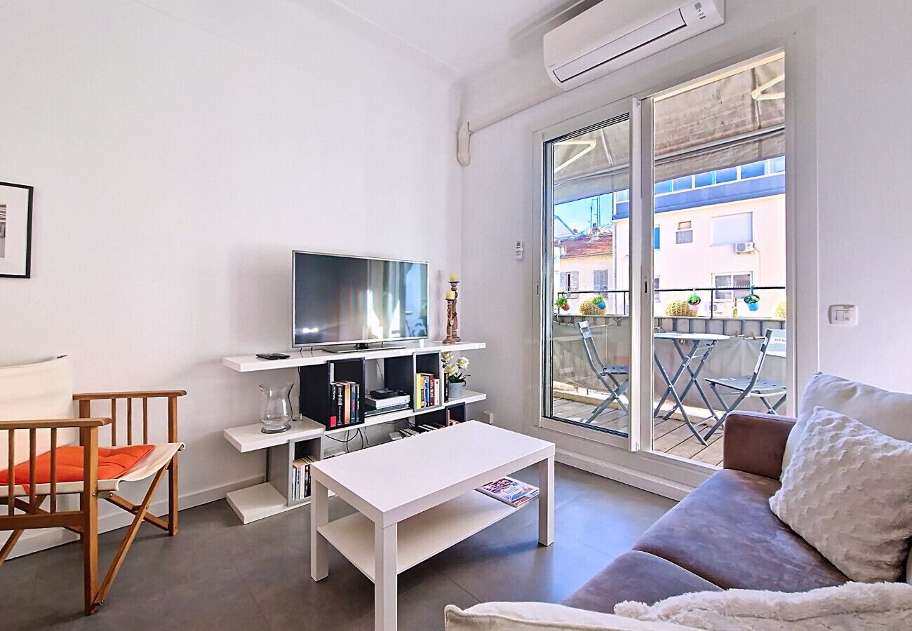 Una sala de estar moderna con un sofá blanco, una mesita pequeña blanca, una silla de madera, un televisor y una estantería.