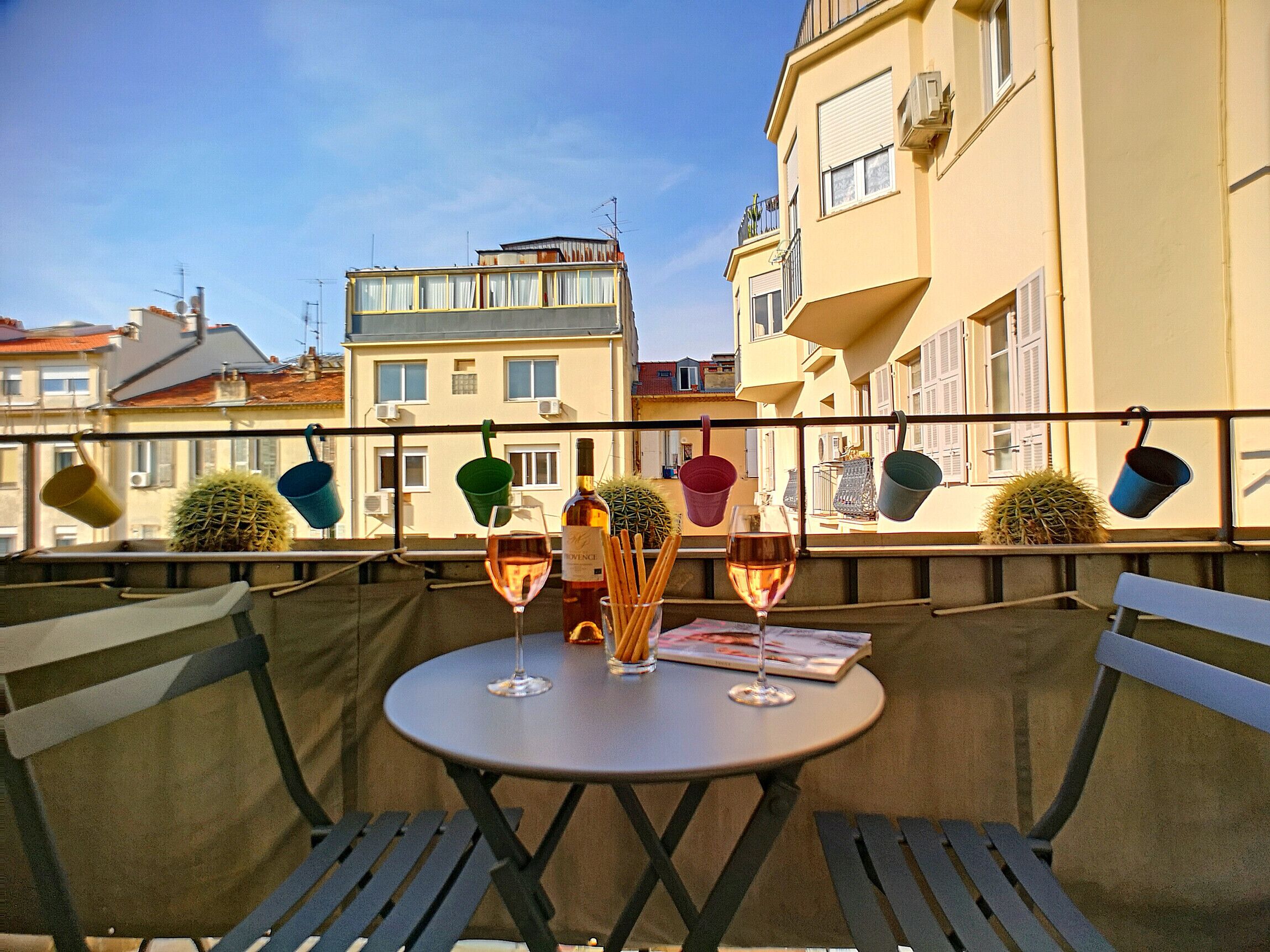 A round table with two chairs on a balcony, two glasses of wine, a bottle of wine, and a menu.