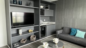 Ein modernes Wohnzimmer mit einem großen Flachbildfernseher, grauen Regalen, einem grauen Sofa mit blauen Kissen und zwei kleinen runden Tischen mit weißen Blumen.