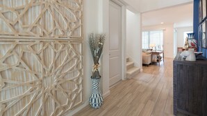 Ein modernes Interieur mit einer geometrischen Holzverkleidung, einer Vase mit Zweigen und einer Treppe, die in einen Essbereich führt.