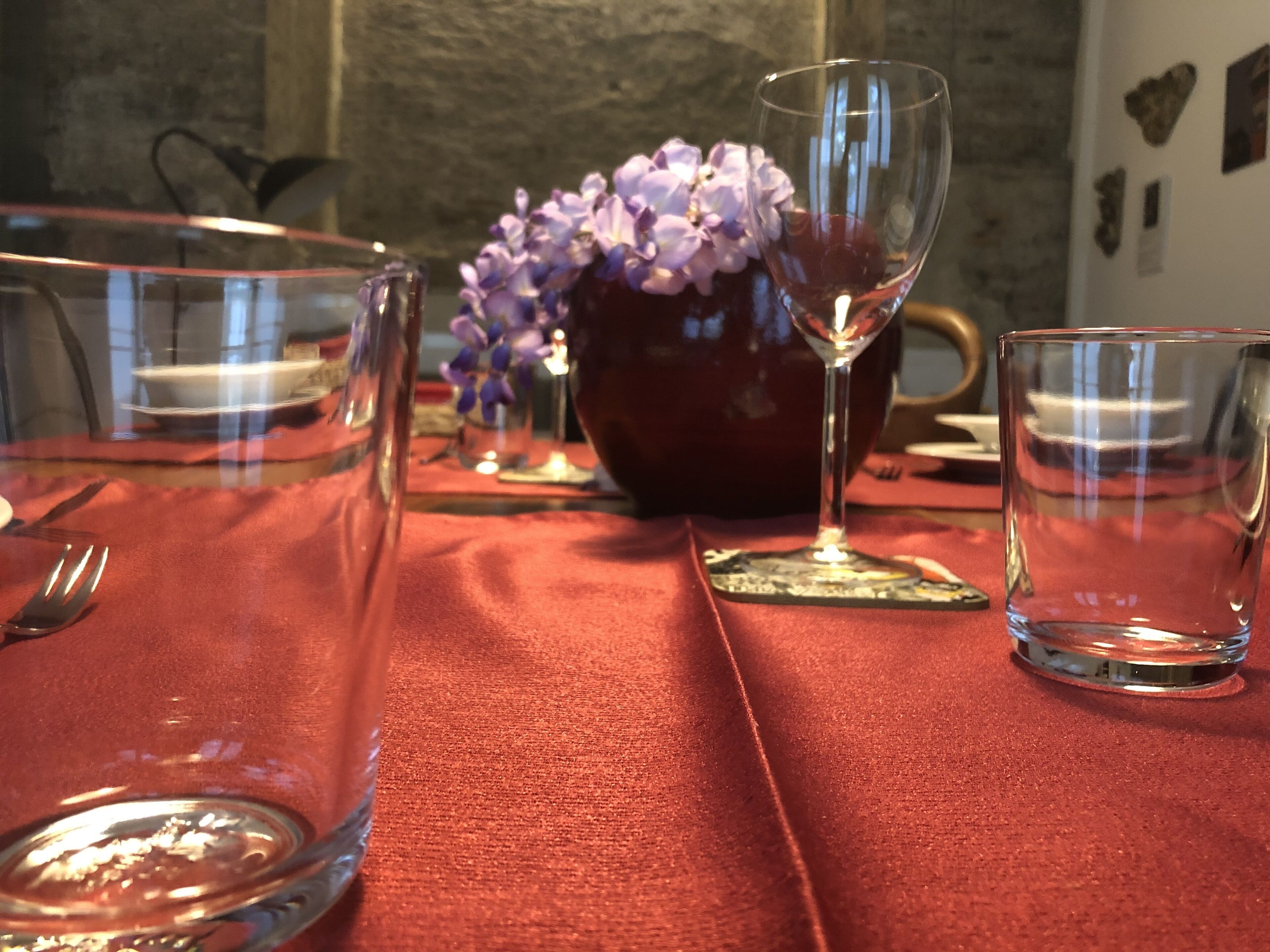 Ein Esstisch mit rotem Tischlein, klarem Glas und einer Vase mit violetten Blumen.