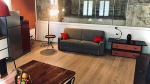 A compact living space with a sofa, a dining table with a fruit bowl, a refrigerator, and a unique brick wall. - Conti house, a cultural experience in the footsteps of Shakespeare (Padova)