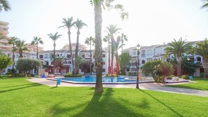 A courtyard with a swimming pool, palm trees, and a building with multiple balconies. - Apartment Aldeas Taray Club 4/5 Admer (La Manga del Mar Menor)