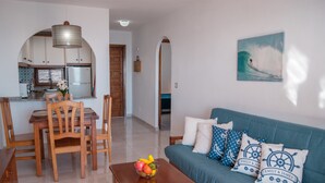 A living room with a sofa, wooden chairs, a dining table with a fruit bowl, and a kitchen visible through an archway. - Apartment Aldeas Taray Club 4/5 Admer (La Manga del Mar Menor)
