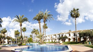 A pool area with palm trees and a building with multiple balconies.