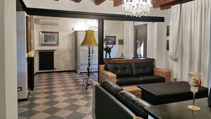 Un salon avec un sol à carreaux, un canapé en cuir noir, un lustre et un coin repas comprenant une table et des chaises.