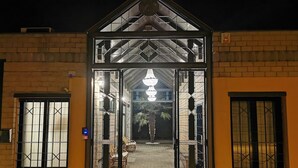 Une entrée d’immeuble avec une porte grillagée, un lustre et un petit patio aménagé avec des chaises.
