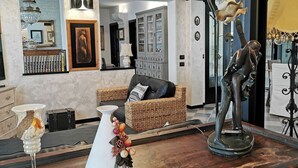 Un salon avec un canapé en osier, un vase blanc contenant un objet décoratif, une statue et un meuble avec des portes en verre.