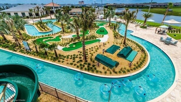 Una piscina con tobogán de agua, rodeada de palmeras y un campo de golf.