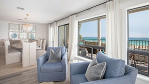 Una sala de estar moderna con un amplio ventanal con vista a la playa, un comedor con mesa redonda y una lámpara de araña.