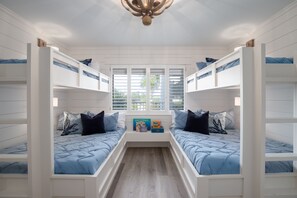 Une chambre avec des lits superposés, une fenêtre avec des stores et un ventilateur de plafond.