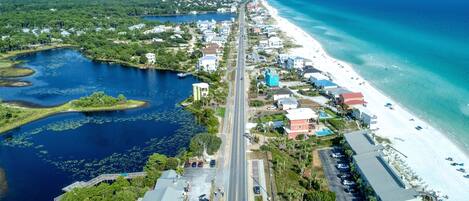 An aerial view of a coastal town with a beach, a marina, and a road running through the center.