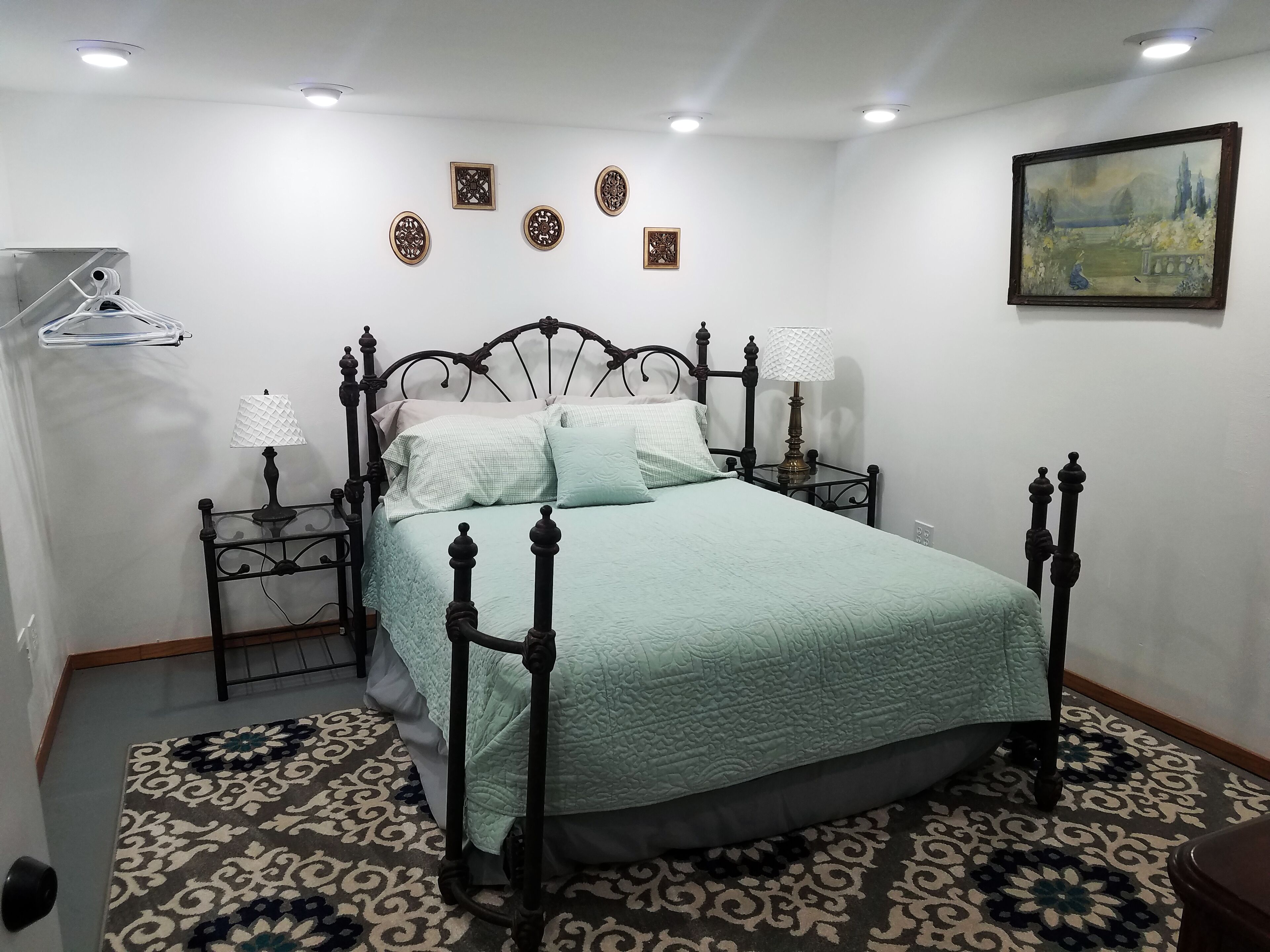 A neatly arranged bedroom with a bed, two bedside tables, a wall-mounted lamp, and decorative wall art.
