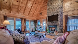 A cozy cabin interior with a stone fireplace, wooden ceiling beams, and a comfortable seating area.
