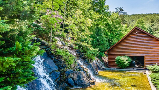A wooden cabin with a waterfall and a pond.