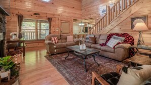 A wooden cabin interior with a living room, a dining area, and a staircase.