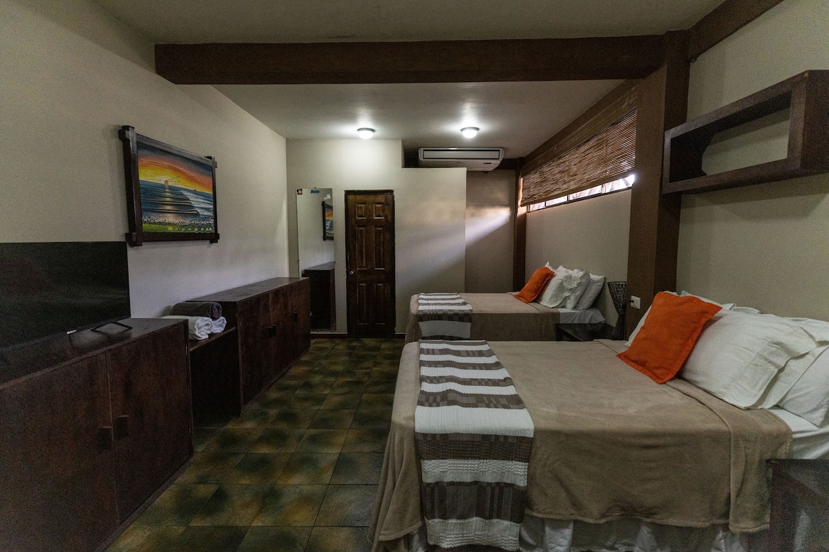 A hotel room with two beds, a TV, a painting, and a wooden floor.
