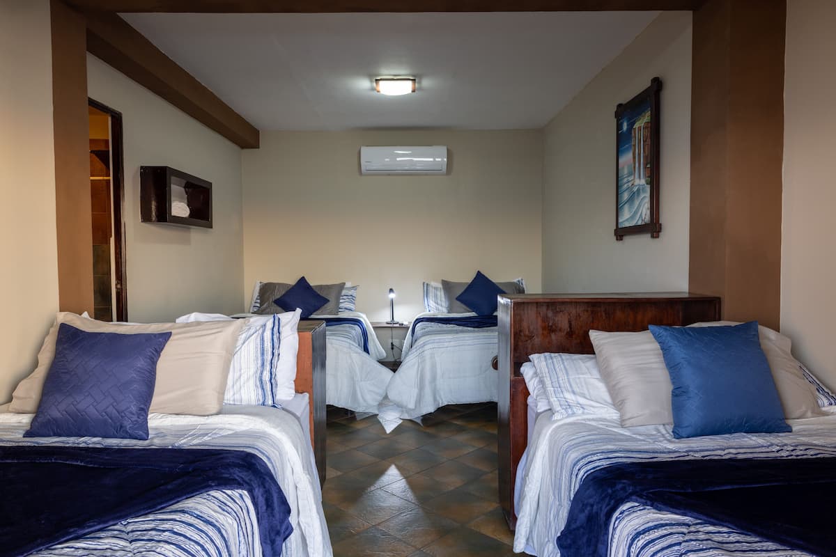 A hotel room with two single beds, a wooden headboard, a nightstand, a bedside table, a wall-mounted air conditioner, and a framed picture on the wall.
