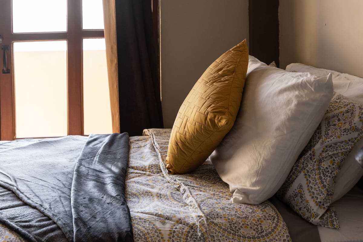 A bedroom with a bed, a window with curtains, and a painting on the wall.