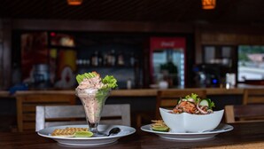 Une scène de restaurant avec une table dressée pour deux personnes, comprenant un dessert présenté dans un récipient en verre transparent et un saladier rempli de salade.