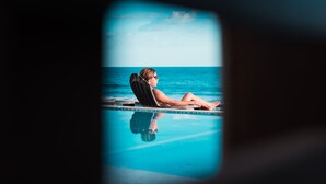 Une personne se détend dans un fauteuil au bord de la piscine, avec vue sur l’océan.