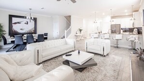 A modern living room with a white sofa, a coffee table, and a dining area with chairs and a table. - Lovely 8Bd Pool Spa Gm Hm Champions Gate-1579pd (Davenport)