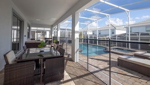 A covered outdoor area with a glass table and wicker chairs, a pool, and a view of neighboring houses. - Lovely 8Bd Pool Spa Gm Hm Champions Gate-1579pd (Davenport)