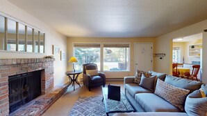 A living room with a fireplace, a sofa, a chair, a table, and a view of the outdoors.