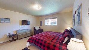 A bedroom with a bed, a television, a dresser, a chair, a window, and wall art.