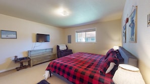Une chambre à coucher comprenant un lit, une télévision, une commode, une chaise, une fenêtre et des œuvres d’art murales.